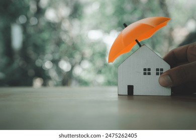 An insurance agent is holding a orange umbrella over a wood house model. Property insurance concept. Protection of housing or house. Security and safety housing insurance Service - Powered by Shutterstock