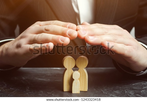 Insurance agent holds hands over family. The\
concept of insurance of family life and property. Family care and\
helping hand concept. Health insurance. Health care. Security and\
Property Protection