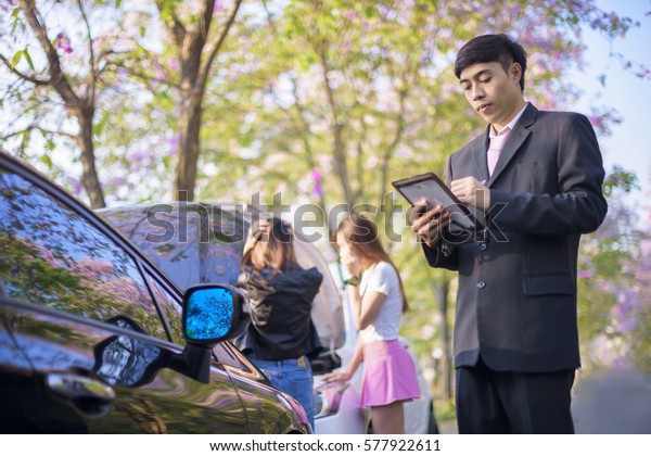 insurance\
agent review and inspect the damage of the car after accident by\
device on line report to office for swift claiming against time\
consumption, both party drivers in background\
