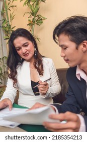 An Insurance Agent Shows A Policy Holder Where To Sign In The Document. A Policy Servicing Agreement.