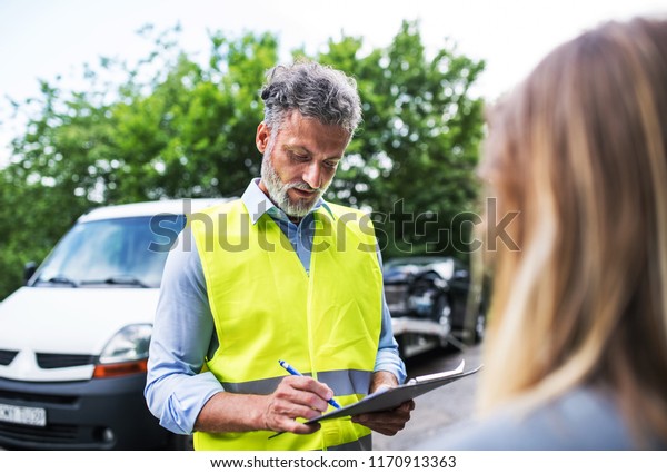 An insurance agent talking to a woman outside\
on the road after a car\
accident.