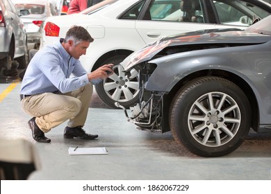 Insurance assessor taking photographs and inspecting a damaged vehicle at a garage.