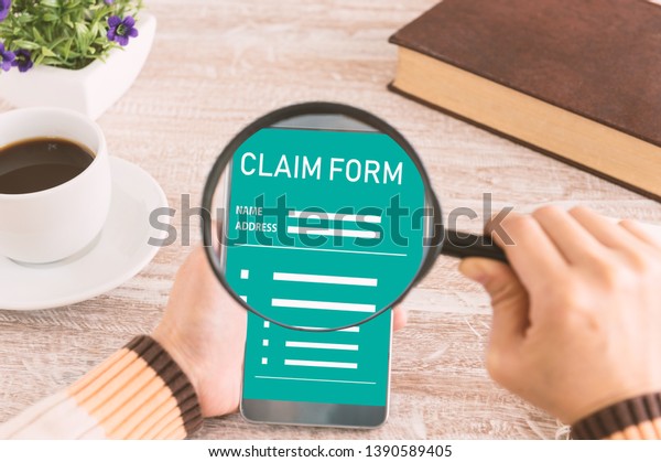 Insurance claims\
concept. People using the use of the magnifying glass screen\
smartphone for claims form on the\
desk.