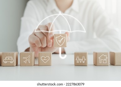 Insurance concept. Protection against a possible eventuality. House, Car, Family, travel and Health on wooden block and Hand holding security icon cover by umbrella icon for life assurance concept. - Powered by Shutterstock