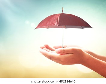 Insurance Coverage Concept: Human Hands Holding Red Umbrella Over Blurred Nature Background