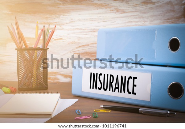 insurance, Office Binder on Wooden Desk.\
On the table colored pencils, pen, notebook\
paper