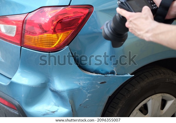 Insurance worker taking photo on camera of dented\
fender on street side for emergency service after car accident.\
Road safety and insurance\
concept