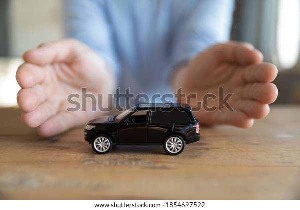 Insurer protecting car with hands, advertising\
automobile insurance coverage services, providing financial\
security for land vehicle against accident, theft. Male goal,\
aspiration buy new auto\
concept