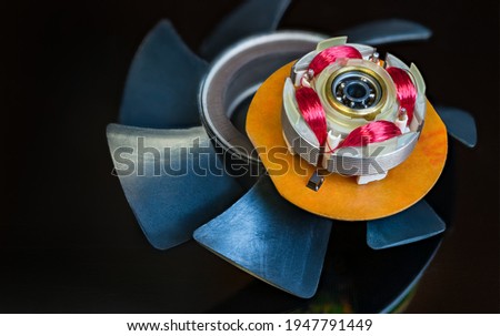Integrated hall sensor in computer fan rotor and plastic vanes on a black background. Red coils copper wire winding and ball bearing in dismantled EC electric motor with electronic commutation system.