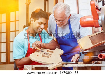Integration of apprentice in guitar maker workshop with a helping master