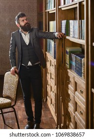 Intellectual elite concept. Aristocrat on busy face looking for book. Man in classic suit stand in vintage interior, library, book shelves on background. Oldfashioned man looking at books, seeking. - Shutterstock ID 1069838657