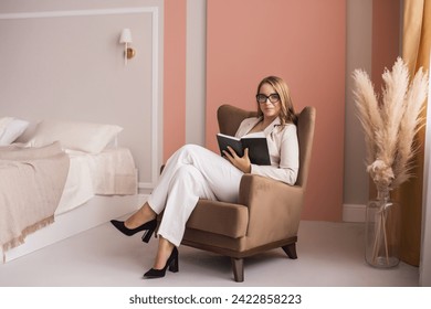 An intellectual woman in elegant workwear absorbed in a book, seated comfortably in a modern chair - Powered by Shutterstock