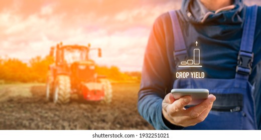 Intelligent agriculture concept with crop yield. Farmer or agrarian with smart phone looking on growing efficiency and crop yield, tractor in background. Smart agriculture and automation concept.