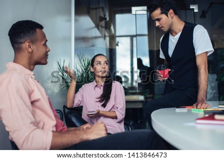 Intelligent business partners sitting in office interior and spending time for brainstorming on information for teamwork, clever diverse male and female discussing plan for startup project