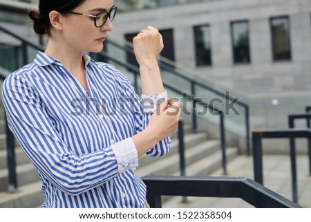 Intelligent business woman with brown hair in glasses in a blue and white striped shirt with white cuffs on her sleevesholding fingers with a button against the background of the city.