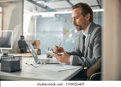 Intelligent businessman working with his notebook and document on desk in modern office - Shutterstock ID 1769355407