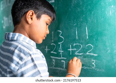 intelligent elementary school kid solving maths problem on chalkboard at classroom -concept of talented, brilliant student and education. - Powered by Shutterstock