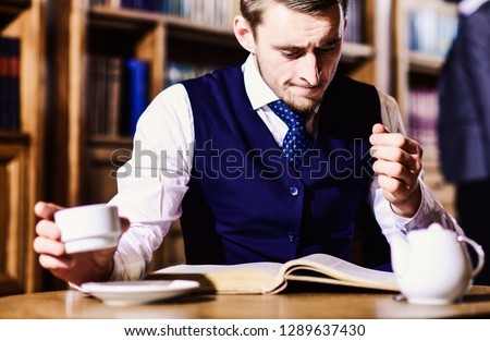 Intelligent, man in suit with good manners hold cup of tea. Five oclock tea tradition concept. Young men with antique bookshelves on background. British elite or aristocrats spend leisure in library.