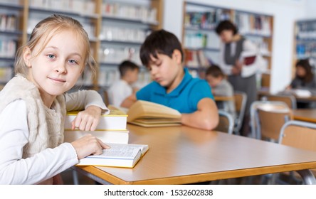 Intelligent Tween Girl Reading In School Library On Background With Other Students And Teacher