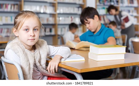 Intelligent Tween Girl Reading In School Library On Background With Other Students And Teacher