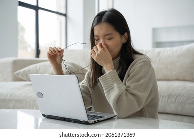 An intense Asian business woman working with glasses, feeling pain in her eyes, overexertion or headache, takes off her glasses and touches the bridge of her nose, the concept of vision problems