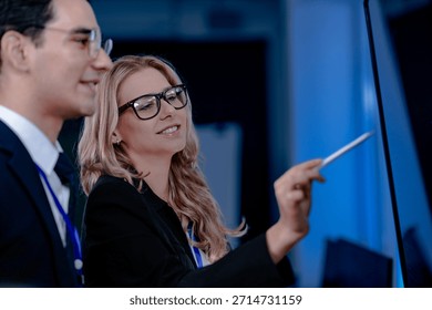 Intense code walkthrough. A female developer uses a stylus pointing to a specific line of code on the screen explaining its function to her male teammate during a debugging session.
