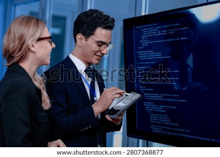 Intense code walkthrough. A female developer uses a stylus pointing to a specific line of code on the screen explaining its function to her male teammate during a debugging session.