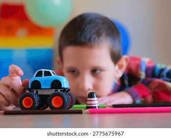 Intense Focus of Young Boy Navigating Blue Toy Monster Truck Through Desk Obstacles — Candid Child Play Photo Featuring Creative Imagination, Fine Motor Skills, and Tabletop Car Games