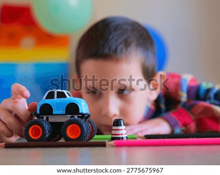 Intense Focus of Young Boy Navigating Blue Toy Monster Truck Through Desk Obstacles — Candid Child Play Photo Featuring Creative Imagination, Fine Motor Skills, and Tabletop Car Games