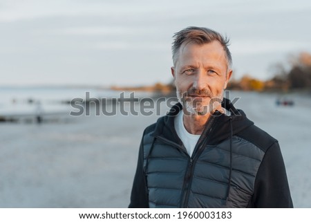 Intense man scrutinising the camera with a penetrating stare outdoors on a desreted beach at dusk in a close up head and shoulders with copyspace