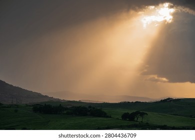 An intense sunset with light illuminating the cloudy sky over a typical Tuscan landscape of green hills and cypress trees, siena, tuscany
