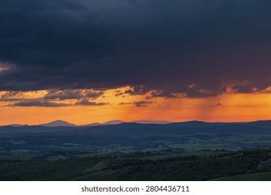 An intense sunset with light illuminating the cloudy sky over a typical Tuscan landscape of green hills and cypress trees, siena, tuscany