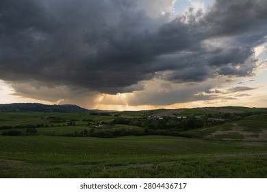 An intense sunset with light illuminating the cloudy sky over a typical Tuscan landscape of green hills and cypress trees, siena, tuscany