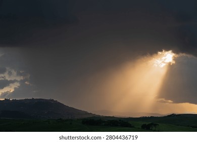 An intense sunset with light illuminating the cloudy sky over a typical Tuscan landscape of green hills and cypress trees, siena, tuscany