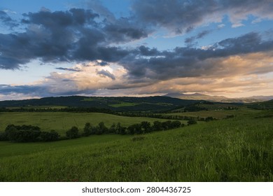 An intense sunset with light illuminating the cloudy sky over a typical Tuscan landscape of green hills and cypress trees, siena, tuscany