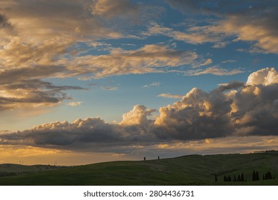 An intense sunset with light illuminating the cloudy sky over a typical Tuscan landscape of green hills and cypress trees, siena, tuscany