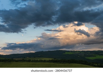 An intense sunset with light illuminating the cloudy sky over a typical Tuscan landscape of green hills and cypress trees, siena, tuscany