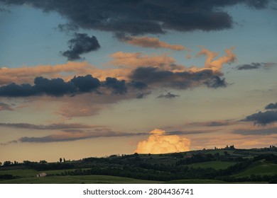 An intense sunset with light illuminating the cloudy sky over a typical Tuscan landscape of green hills and cypress trees, siena, tuscany