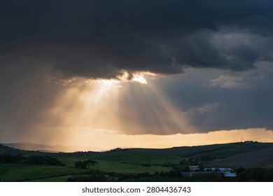 An intense sunset with light illuminating the cloudy sky over a typical Tuscan landscape of green hills and cypress trees, siena, tuscany