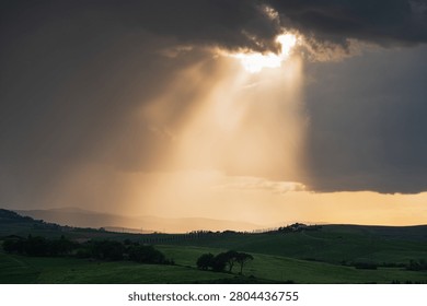 An intense sunset with light illuminating the cloudy sky over a typical Tuscan landscape of green hills and cypress trees, siena, tuscany