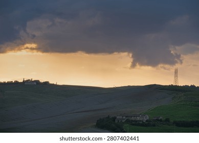 An intense sunset with light illuminating the cloudy sky over a typical Tuscan landscape of green hills and cypress trees, siena, tuscany
