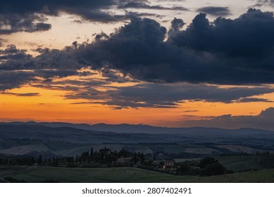 An intense sunset with light illuminating the cloudy sky over a typical Tuscan landscape of green hills and cypress trees, siena, tuscany