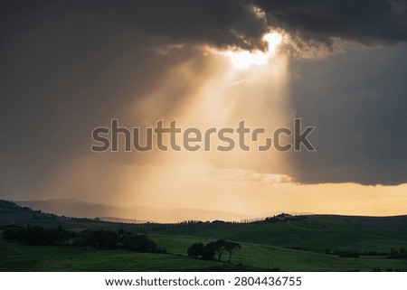 An intense sunset with light illuminating the cloudy sky over a typical Tuscan landscape of green hills and cypress trees, siena, tuscany
