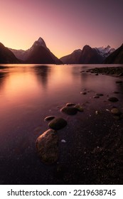 Intense twilight colors glow in the clear morning sky over the Milford Sound of New Zealand in the Fiordland National Park.