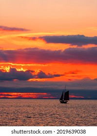 Intense, Vibrant Orange Sunset, And A Sailboat (sloop?) With Two Sails In Silhouette In The Distance. Long Island Sound Between Connecticut And New York State's Long Island.