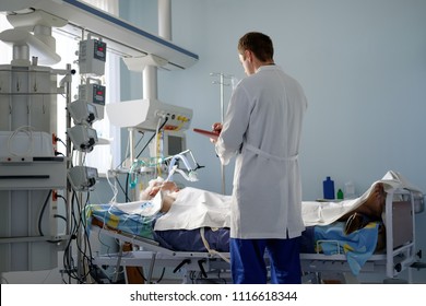 intensive care caucasian doctor examines intubated critical stance patient writing notes to case report in intensive care department