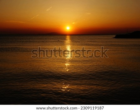 Intensive dusk sunset on the seaside with fiery red sky and sun in the center above wavy sea surface