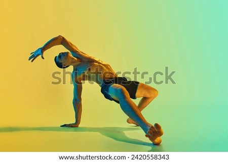 Intensive full-body training. Muscular athletic young shirtless man, with fit body doing workout exercises against gradient blue yellow background in neon. Active and healthy lifestyle, sport concept