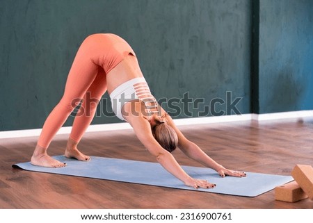 Intensive yoga training in studio flexible woman in sportswear stretches body standing in pose Downward facing dog on blue mat active person enjoying exercise taking care of health