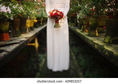 Intentionally Blurred Image Of A Bride In White Simple Dress Hold A Bouquet Of Red Flowers In Her Hands. Tilt-shift Lens Used, Soft Selective Focus.